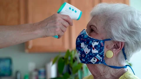 Hand aims digital thermometer at forehead of senior elderly woman wearing face Vídeos de archivo 136375389