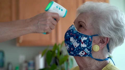 Hand aims digital thermometer at forehead of senior elderly woman wearing face Stock Footage 136375582