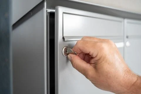 Hand and  mailbox with a key in a row of grey metal mailboxes with drop slots Stock Photos