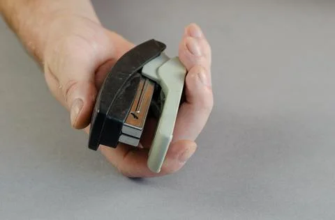 Hand and stapler on gray background. A man holding a plastic paper stapler. P Stock Photos
