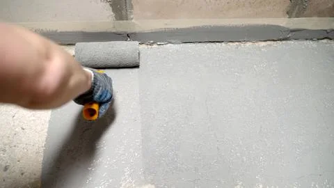 Hand applying gray paint with roller on concrete floor Stock Photos