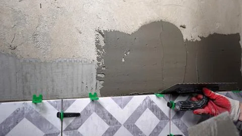 Hand applying gray tile adhesive to wall above patterned ceramic tiles with.. Stock Photos