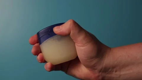 Hand applying petroleum jelly from a small blue container for skin care Stock Footage 340266751