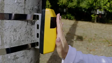 Hand approaches a yellow electronic device mounted on a pole, capturing the Stock Footage 327641036
