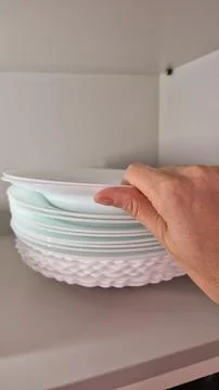 A hand arranges white plates on a kitchen shelf during domestic chores. Stock Photos