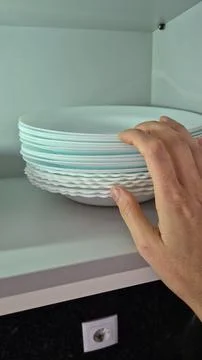A hand arranges white plates on a kitchen shelf during domestic chores. Stock Photos