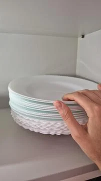 A hand arranges white plates on a kitchen shelf during domestic chores. Stock Photos
