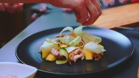 Hand arranging cucumber and mango slices on salad in kitchen Vidéo 342857806