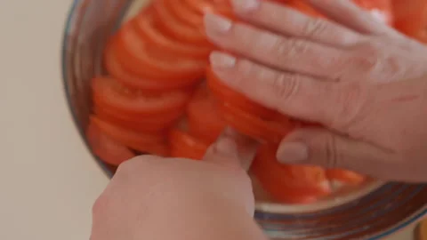 Hand arranging thin tomato slices into metal bowl during kitchen preparation Stock Footage 347618626
