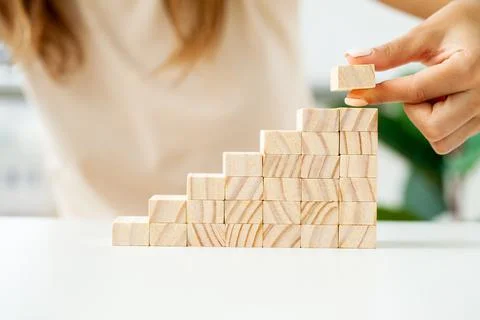 Hand arranging wood cube stacking as stair step shape Stock Photos