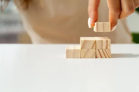 Hand arranging wood cube stacking as stair step shape Stock Photos