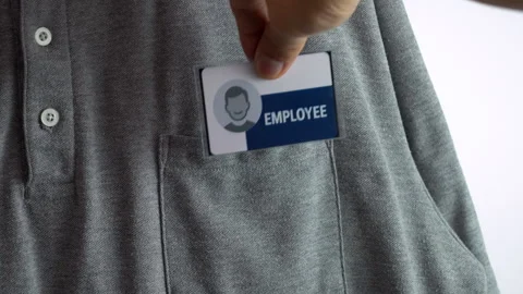 A hand attaches a blue and white employee tag to a gray button-down shirt pocket Stock Footage 318969404