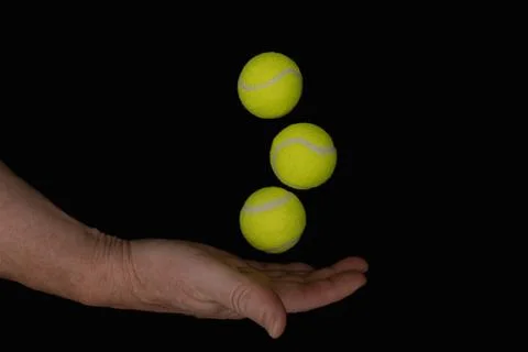Hand balancing three bright yellow tennis balls on black background Stock Photos
