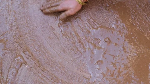 Hand with bangles applying wet mud coating on rural floor Видео 330660986