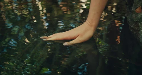 A hand barely touches the surface of a clear rippling pool of cenote in the Stock Footage 311964122