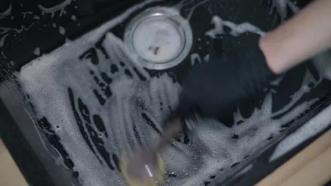 A hand in a black glove scrubs a surface with a brush and bubbles made from Stockbeeldmateriaal 337642864