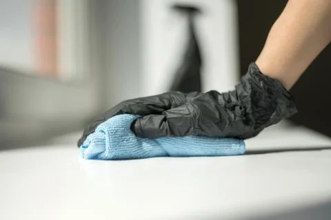 A hand in black gloves holds a microfiber cleaning cloth and a spray with Stock Photos