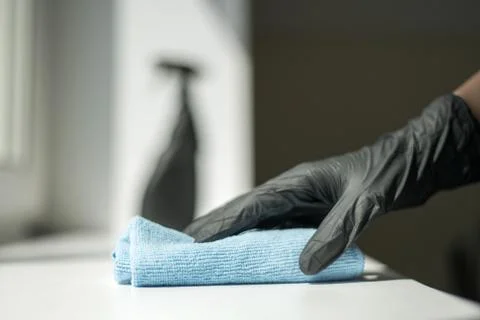 A hand in black gloves holds a microfiber cleaning cloth and a spray with Stock Photos