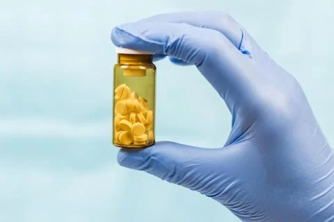Hand in blue glove hold yellow jar with pills Stock Photos