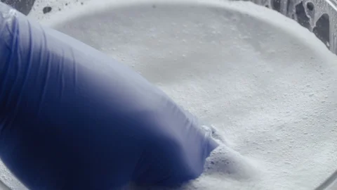 The hand in the blue glove interferes with soapy water with powder Stock Footage 89810472