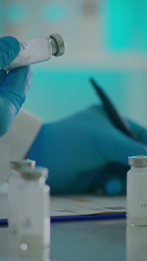Hand with blue gloves preparing to label vaccine vials in a laboratory setti Stock Footage 331596825