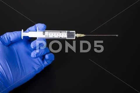 A Hand With A Blue Medical Glove Is Holding A Syringe