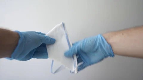Hand in blue nitrile gloves holding mask sharing protective respirator. Stock Footage 127219169