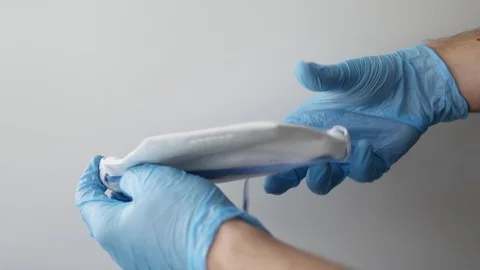 Hand in blue nitrile gloves holding mask sharing protective respirator. Stock Footage 127219289