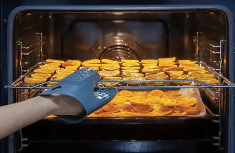 A hand in a blue oven mitt pulls a wire rack from a warm oven Stock Photos