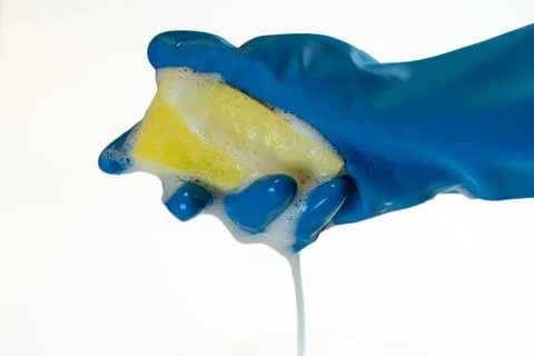 A hand in a blue rubber glove squeezing a dish sponge, with soap and foam d.. Stock Photos