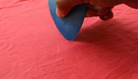 A hand with blue triangle tailor chalk to draw marking on a red cloth Foto stock