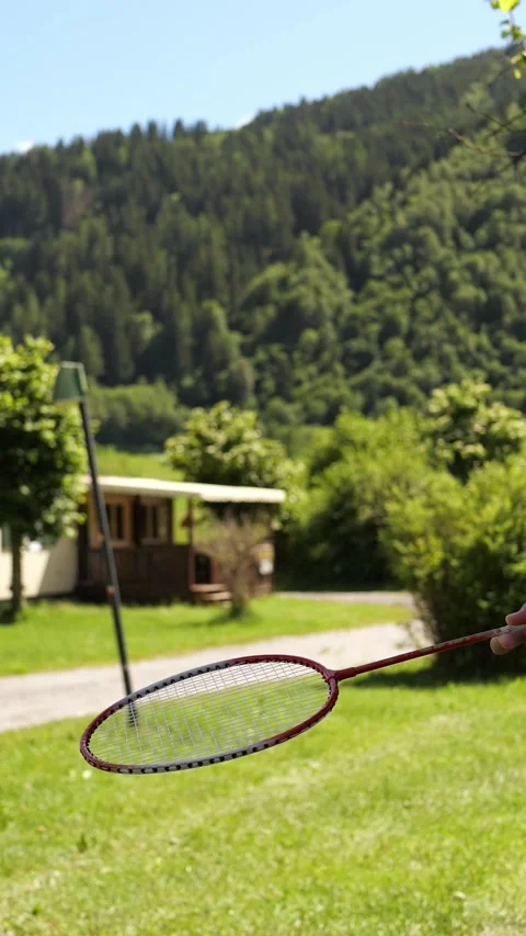 Hand bouncing shuttlecock on badminton racket over sunny mountain lawn Stock Footage 343571701