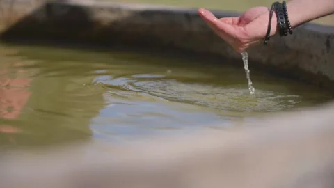 Hand with bracelets cups water over a stone pool 動画素材 337638640