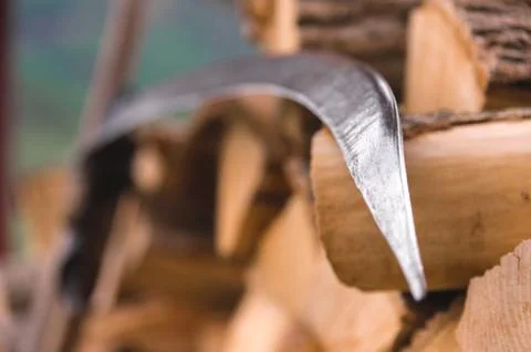 A hand braid for mowing grass and hay stands near the stacked firewood poked Stock Photos