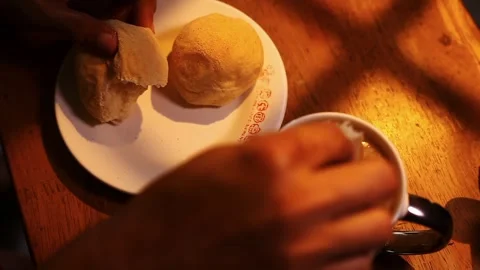 Hand breaking of a piece of Filipino bread called Pandesal and dipping it into Stock Footage 336032834
