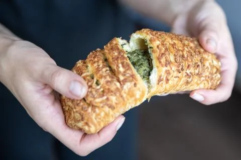 A hand breaks a spinach bun in half close-up. Eating quick snacks. Stock Photos
