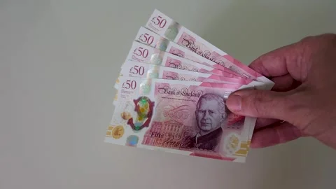Hand brings five £50 notes totalling £250 into centre frame, slow motion Stock Footage 334231207