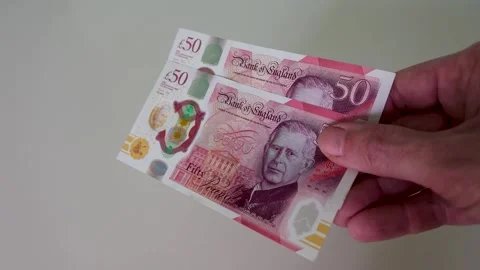 Hand brings two £50 notes into centre frame and holds them, slow motion Stock Footage 334231216