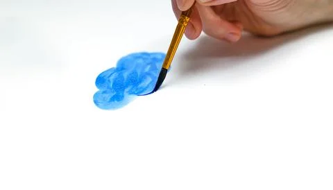Hand with brush drawing blue cloud with watercolor paints on white paper. Stock Photos