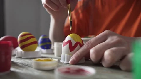Hand with a brush is drawing a colored pattern on an Easter egg. Stock Footage 176860491