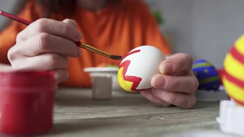 Hand with a brush is drawing a colored pattern on an Easter egg. Stock Footage 176861095