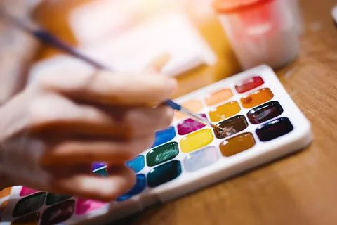 Hand with brush for drawing over multi-colored palette of watercolor paints Stock-Fotos