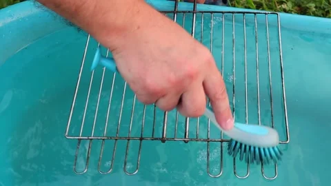 A hand with a brush washes the grill grate slowly in a blue basin Vidéo 139336525