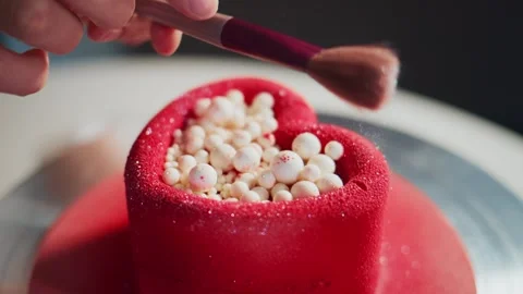 Hand brushes fine sugar over a red cake shaped like a heart Stock Footage 336082064