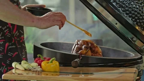 Hand brushing roasted whole chicken on a the grill bbq barbeque kamado camado Stock Footage 292810197