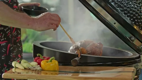 Hand brushing roasted whole chicken on a the grill bbq barbeque kamado camado Stock Footage 292810395