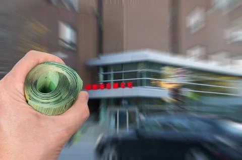 Hand with bunch of bank notes in front of hospital emergency entrance Stock Photos