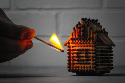 Hand with a burning match sets fire to the house model of matches, risk, prop Stock Photos