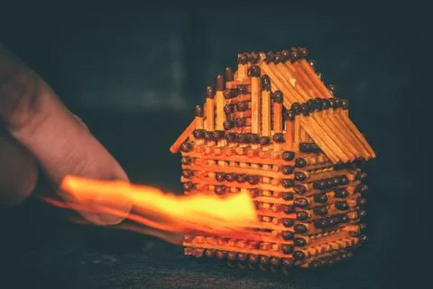 Hand with a burning match sets fire to the house model of matches, risk, prop Stock Photos