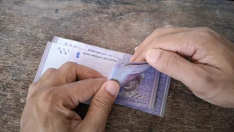 Hand calculates the banknote Ringgit Malaysia, value of the 100 on the wooden ta Stock Footage 128407190